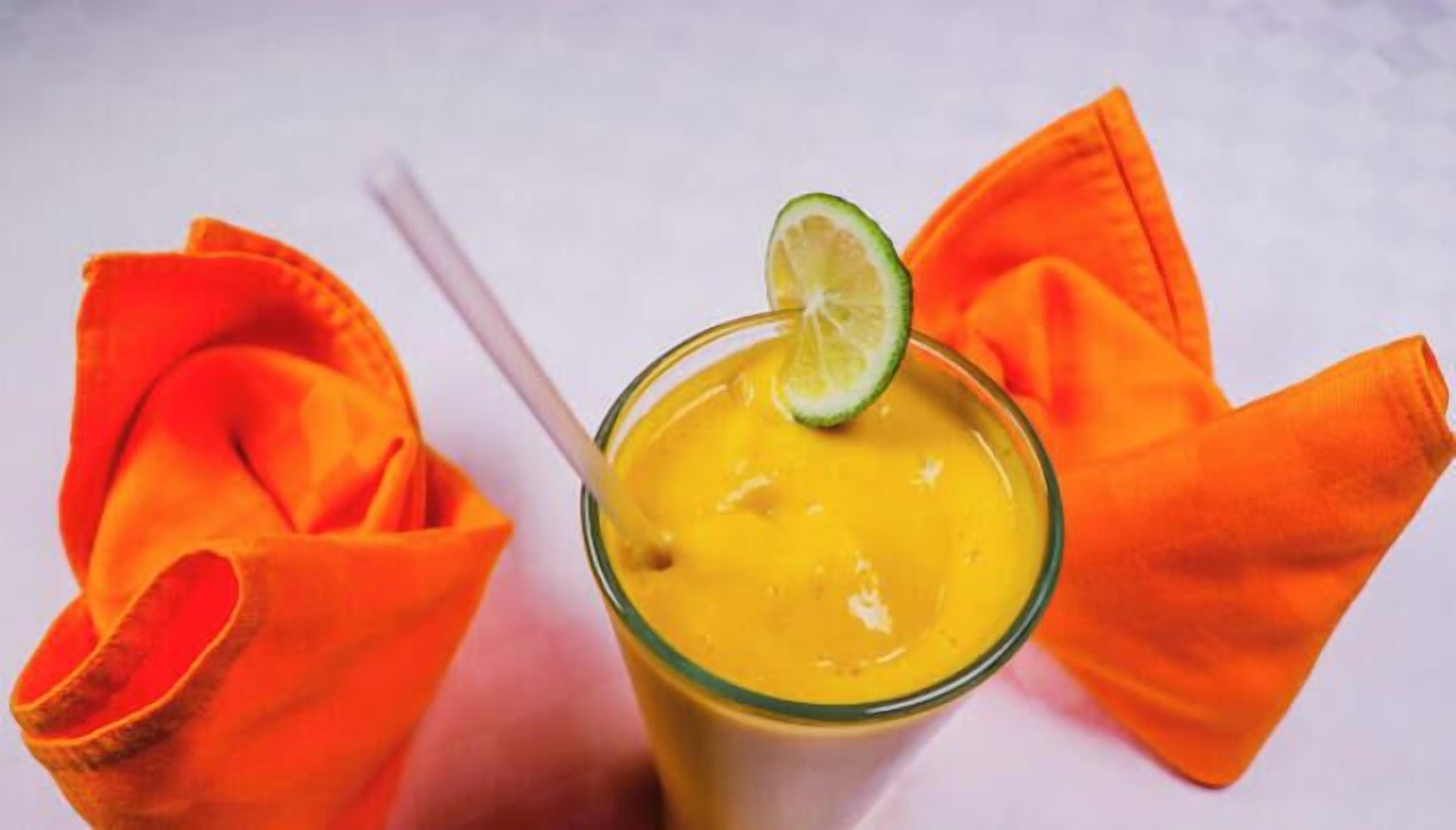 A glass of yellow beverage with a lime garnish, accompanied by orange napkins.