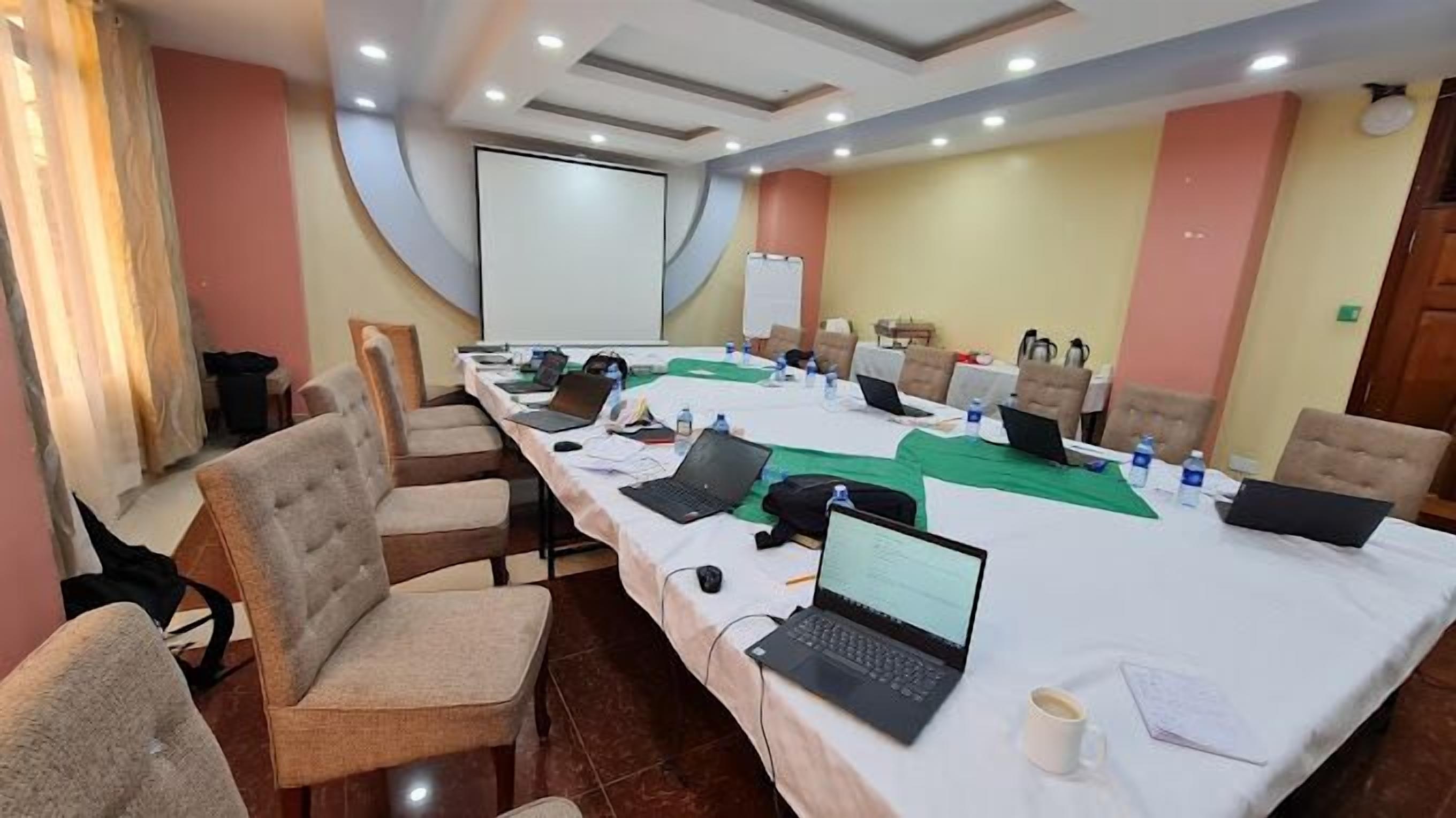 Un salón de conferencias con una larga mesa, varias sillas, computadoras portátiles y botellas de agua.
