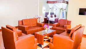 A hotel lobby with leather sofas arranged around a central coffee table, a bed with a canopy in the background, and a TV mounted on the wall. - Maxland Hotel Juja (Juja)