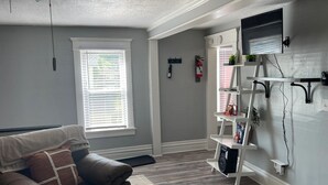 A living room with a sofa, a white wall-mounted TV, and a white shelving unit with various items.