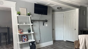 A living room with a white bookshelf, a flat-screen TV mounted on the wall, and a door leading to another room.