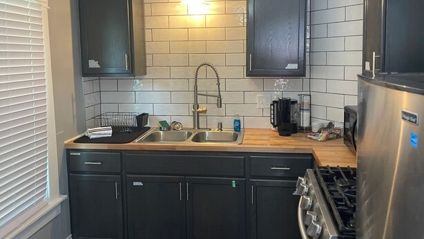 A modern kitchen with dark cabinets, a stainless steel sink, a coffee maker, and a refrigerator.
