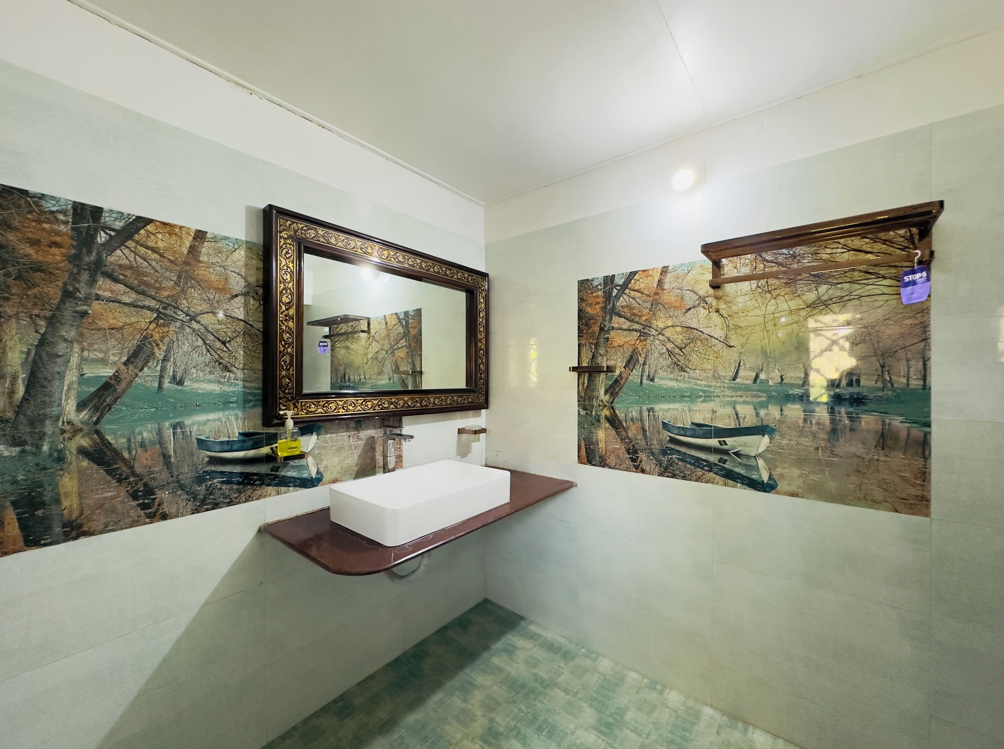 A bathroom with a white sink, a mirror, and two wall-mounted picture frames depicting a forest scene.