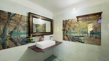 A bathroom with a white sink, a mirror, and two wall-mounted picture frames depicting a forest scene.