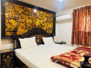 Une chambre d’hôtel dotée d’un grand et somptueux panneau de tête de lit orné d’une peinture détaillée représentant des éléphants et de la végétation. Le lit est recouvert de draps blancs et d’une couverture à motifs floraux.