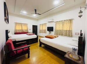 Une chambre d’hôtel avec deux lits, un ventilateur de plafond, un appareil de climatisation, une télévision et une petite table avec une carafe.