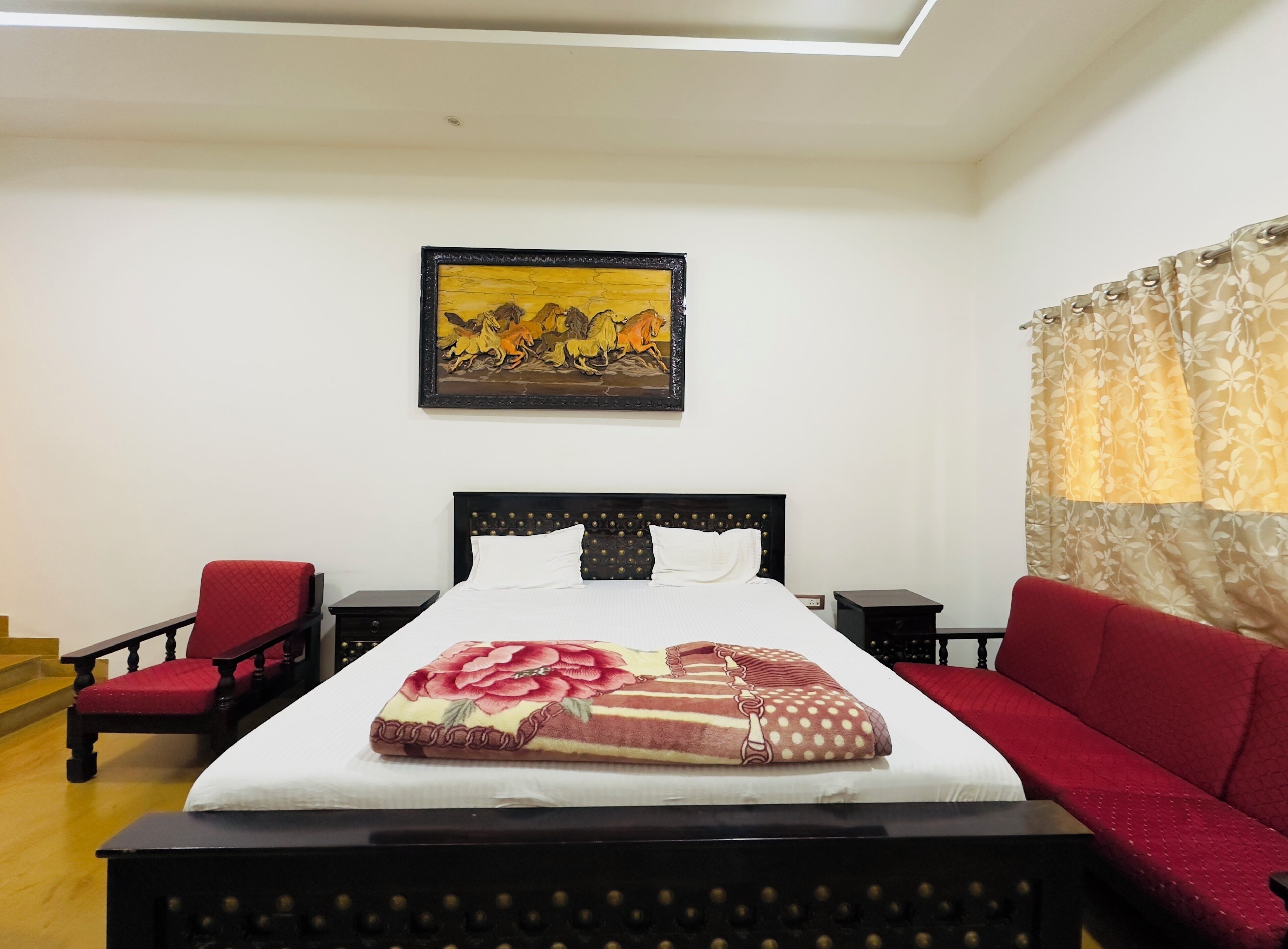 Een keurig ingerichte hotelkamer met een bed, een rode fauteuil, een tafeltje en een schilderij aan de muur.