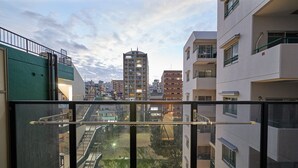 Un balcó amb vista a un paisatge urbà, incloent un edifici alt i altres edificis residencials.