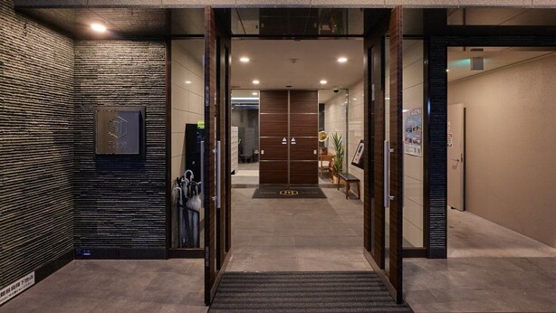 Entrada d'un hotel modern amb una porta de vidre, una taula de recepció i un cartell fixat a la paret.