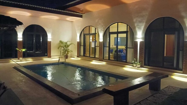 A swimming pool with a bench, surrounded by arched windows and a brick wall.