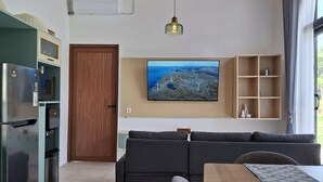 A modern kitchen with a built-in fridge, microwave, and water dispenser. There is a wooden ceiling, a large TV mounted on the wall, and a dining area with a table and chairs.