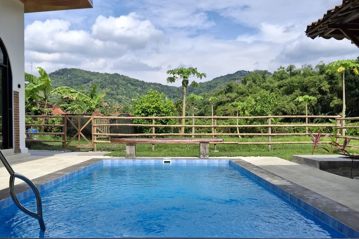Una piscina con cubierta de madera y vista a un paisaje verde exuberante y colinas al fondo.