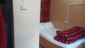 Una cama individual con cabecera de madera, ropa de cama blanca y una colcha roja estampada.