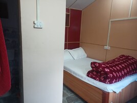 Una cama individual con cabecera de madera, ropa de cama blanca y una colcha roja estampada.