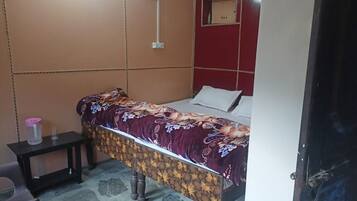 Una habitación pequeña con una cama individual, un edredón estampado con flores, una mesita de noche con lámpara y una pared de acento roja.