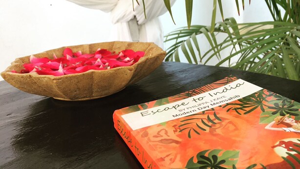 A book titled 'Escape to India' by Philip J. Kayesahib on a table next to a bowl filled with red flower petals.