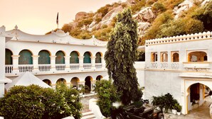 A traditional building with multiple balconies and arched windows, surrounded by lush greenery and a rocky hillside.