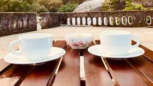 A wooden table with two white cups and a floral bowl, set against a backdrop of rocky hills and sparse vegetation. - Rawla Bisalpur (Bali)
