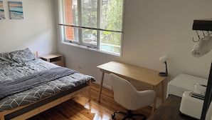 Une chambre à coucher comprenant un lit, un bureau, une chaise, un radiateur et une fenêtre avec des stores.