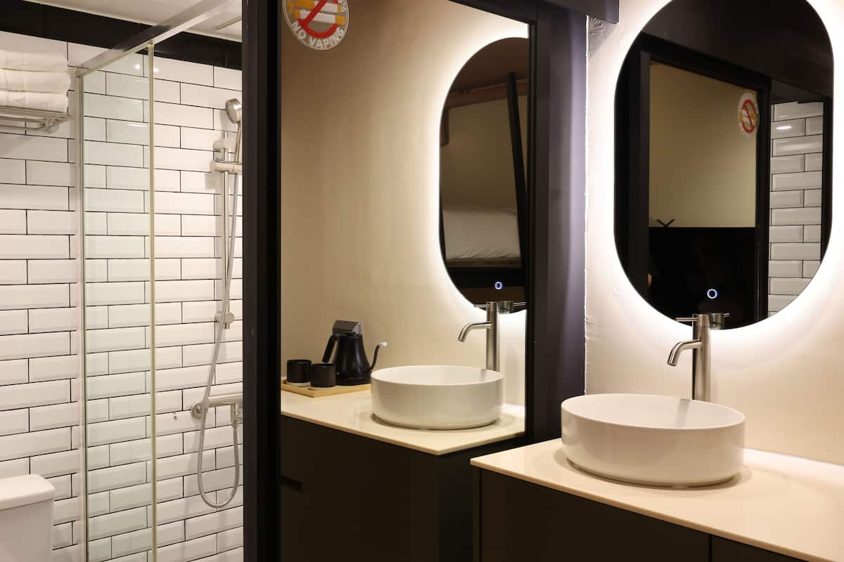 Un baño moderno con ducha de azulejos blancos, lavabo de forma redonda y espejo con marco circular.