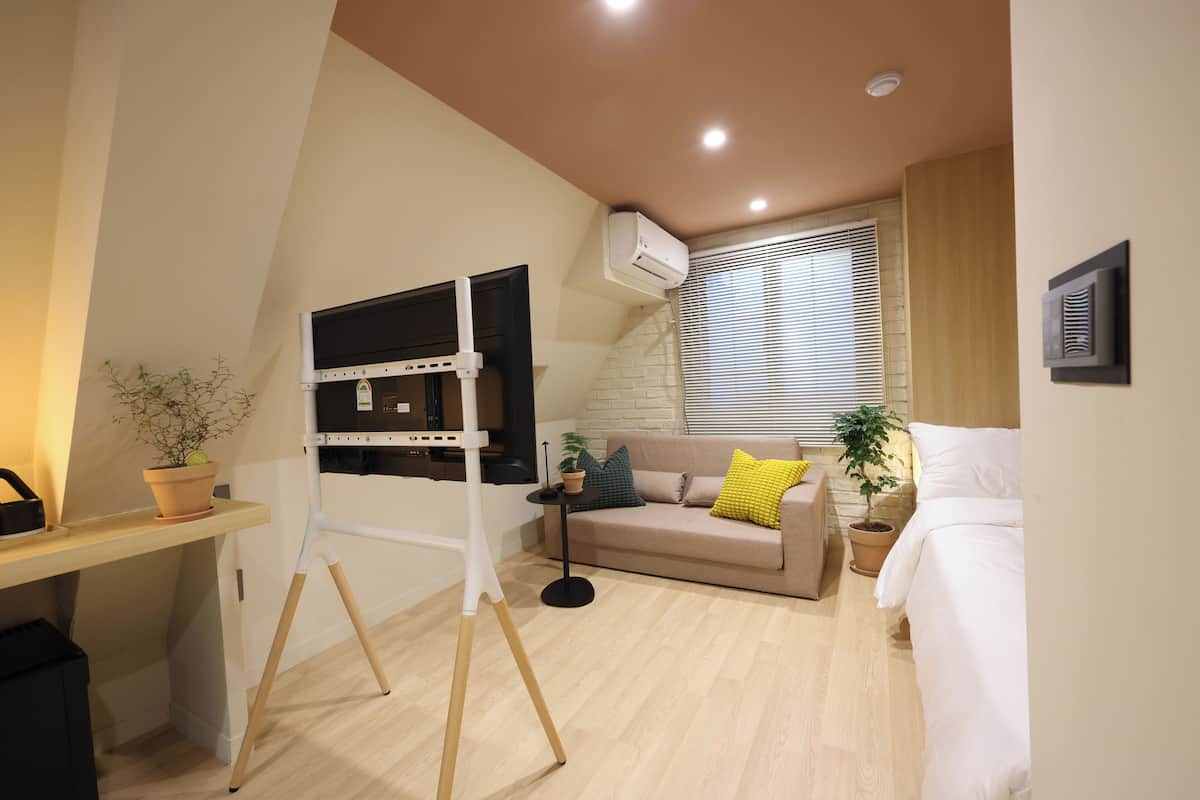 Un espacio habitable compacto con kitchenette, un sofá con cojines, una cama y una planta en maceta.