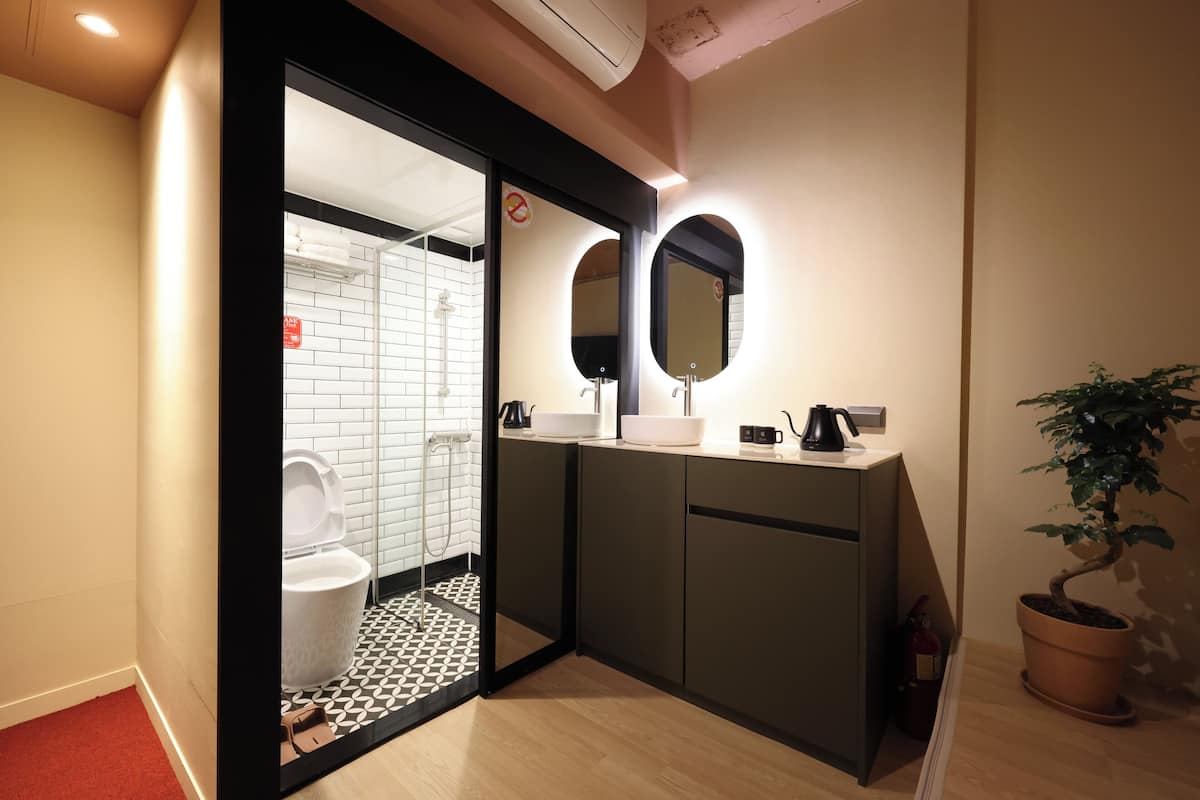 Un baño moderno con inodoro, bidé y lavamanos. Hay dos espejos sobre el lavamanos, y se ve una planta en maceta.