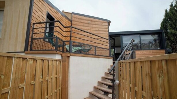 A modern building with a wooden exterior, a staircase leading to a balcony, and a large window. - Cocoon under the oaks with jacuzzi (Saint-Martin-de-Londres)