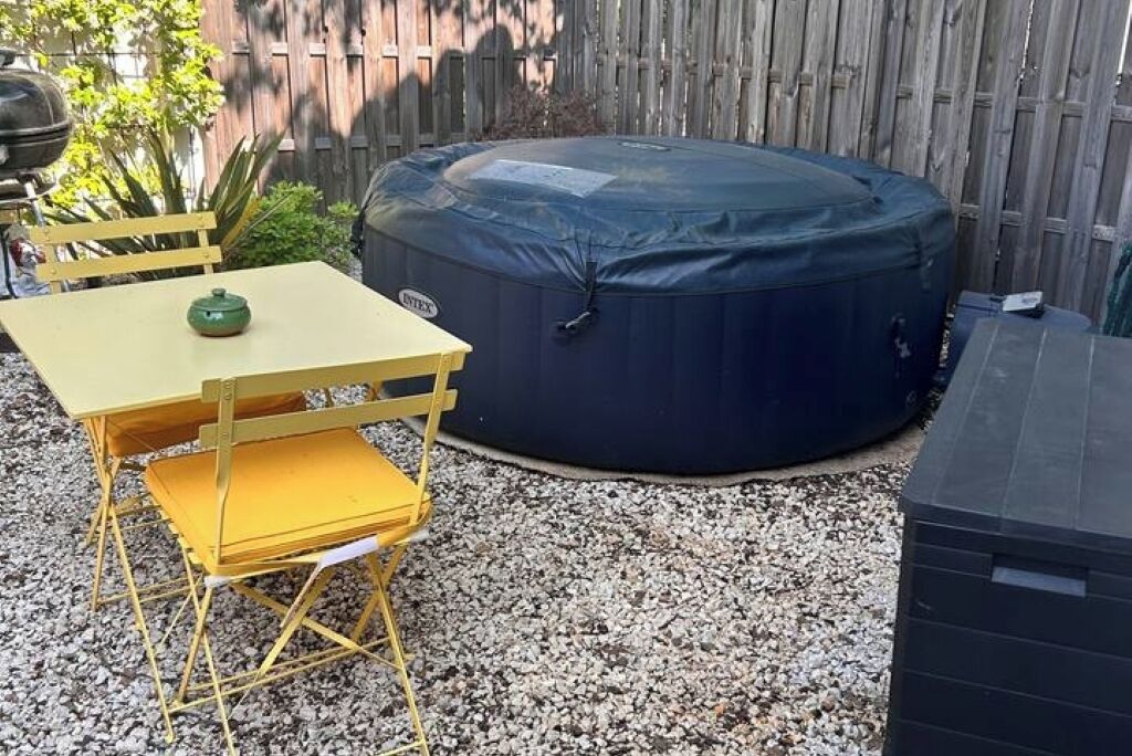 En terrasse med en rund, mørk udendørsvarmeovn, et gult bord med en grøn genstand på, og gule stole.