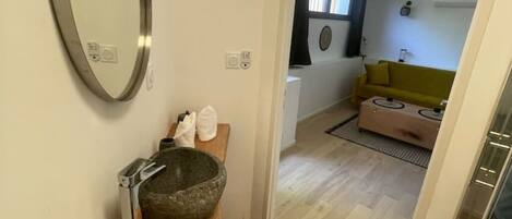 A modern bathroom with a stone basin, a mirror, and a wooden vanity.