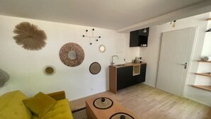 A modern living room with a yellow sofa, a wooden coffee table, and a kitchen area with a black countertop and white cabinets. - Cocoon under the oaks with jacuzzi (Saint-Martin-de-Londres)