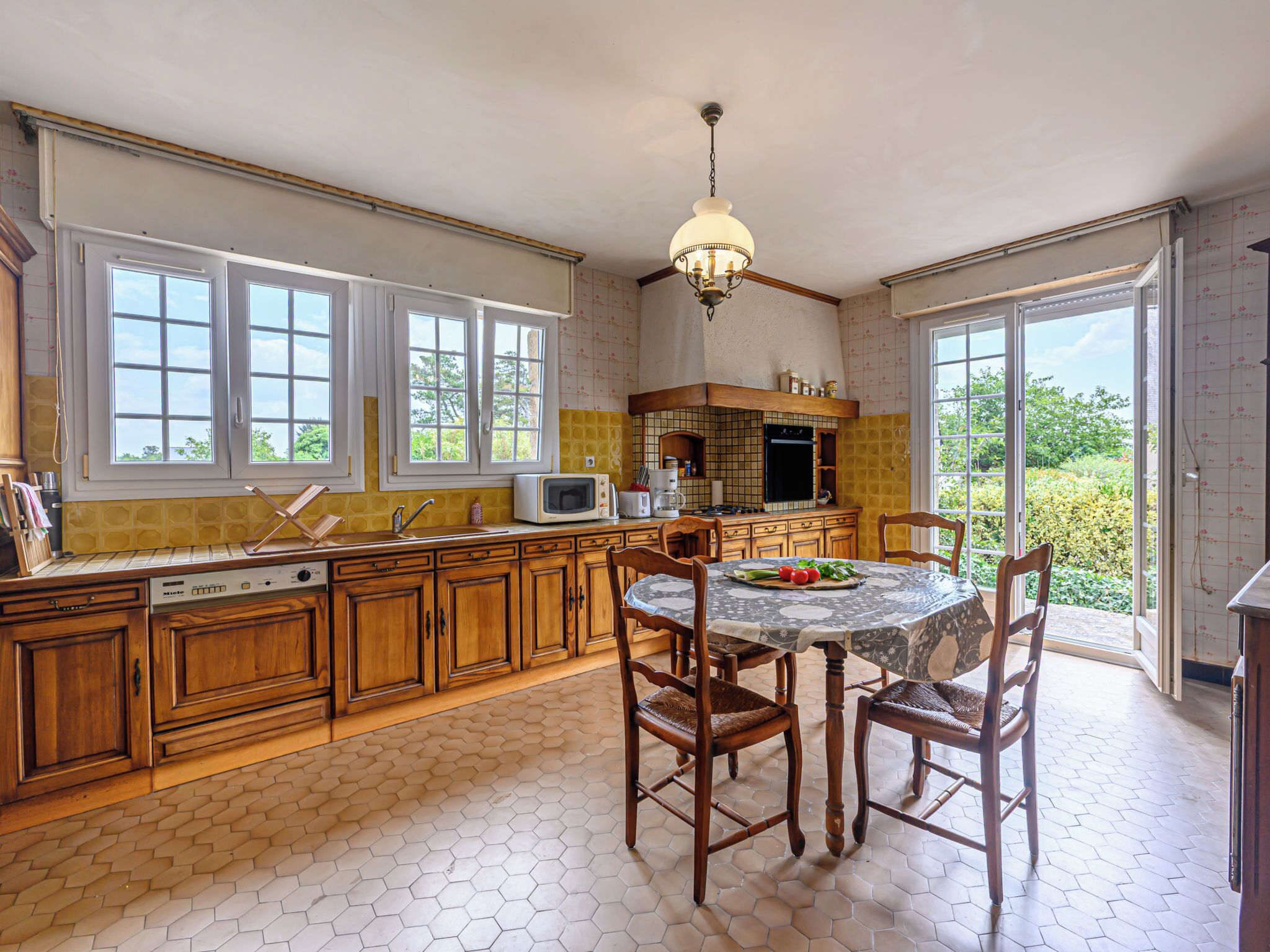 Una cocina con armarios de madera, una mesa de comedor con sillas, un microondas y una ventana con vistas a la vegetación.