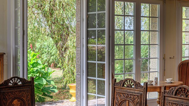 Un coin repas avec une table dressée pour quatre personnes, une grande fenêtre donnant sur un jardin et une porte menant à l’extérieur.