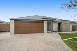 A modern single-story house with a garage, a stone exterior wall, and a small front yard. - 4BR Retreat w/ BBQ & Sleeps 8+ (Byford)