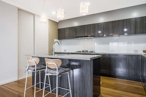 A modern kitchen with a central island, bar stools, a stainless steel sink, and pendant lighting. - 4BR Retreat w/ BBQ & Sleeps 8+ (Byford)