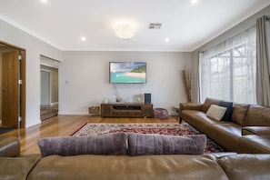 A living room with a flat-screen TV, leather sofas, a patterned rug, and a wooden entertainment unit. - 4BR Retreat w/ BBQ & Sleeps 8+ (Byford)