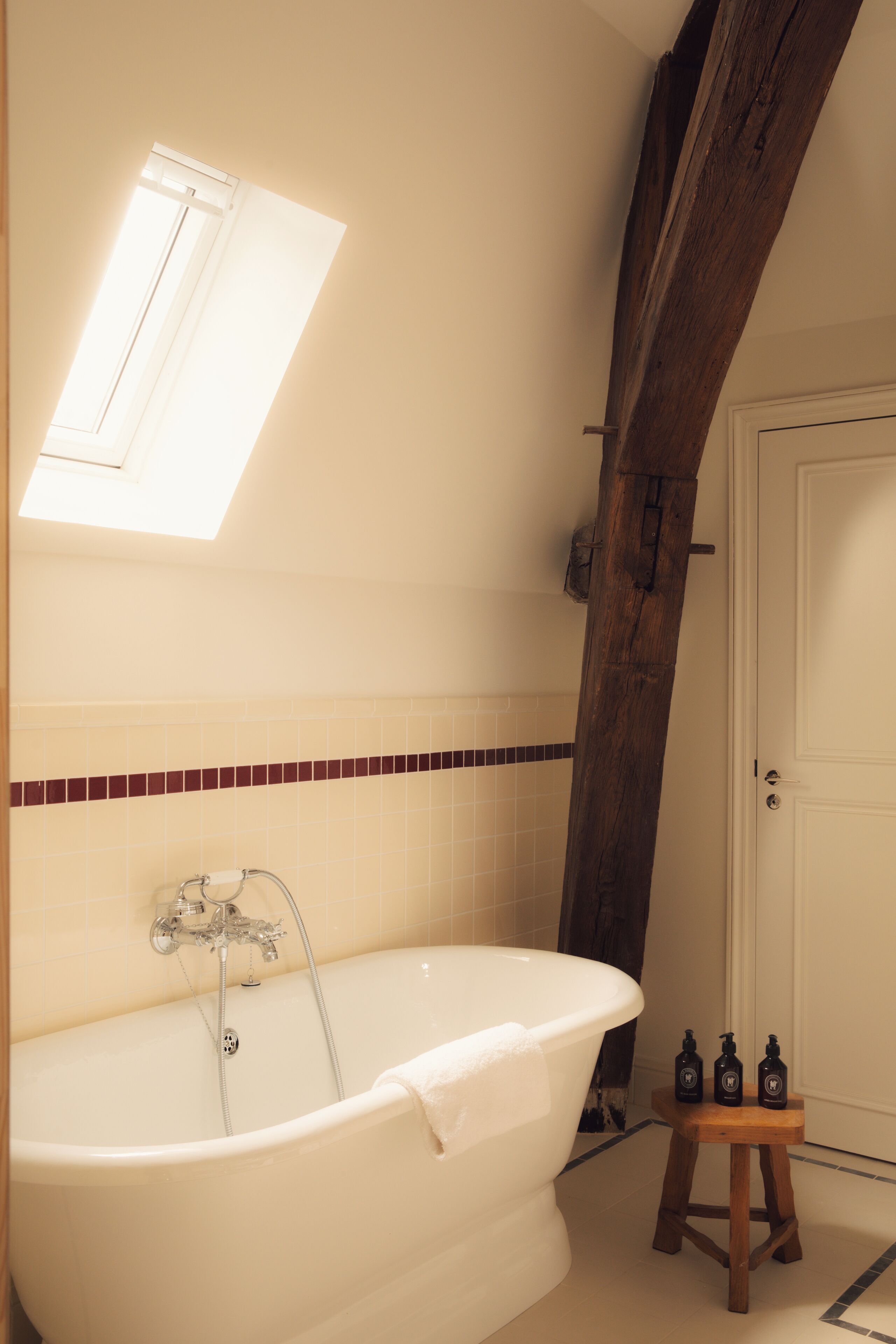 A bathroom with a freestanding bathtub, a small wooden stool, and a window above the tub.