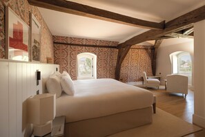 A bedroom with a large bed, a desk, and a chair, with patterned wallpaper and wooden beams. - Les Sources de Vougeot (Gilly-lès-Cîteaux)