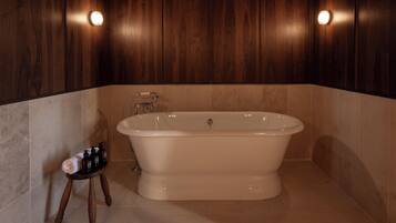 Een badkamer met een vrijstaand bad, houten wandbekleding en een klein krukje met toiletartikelen.