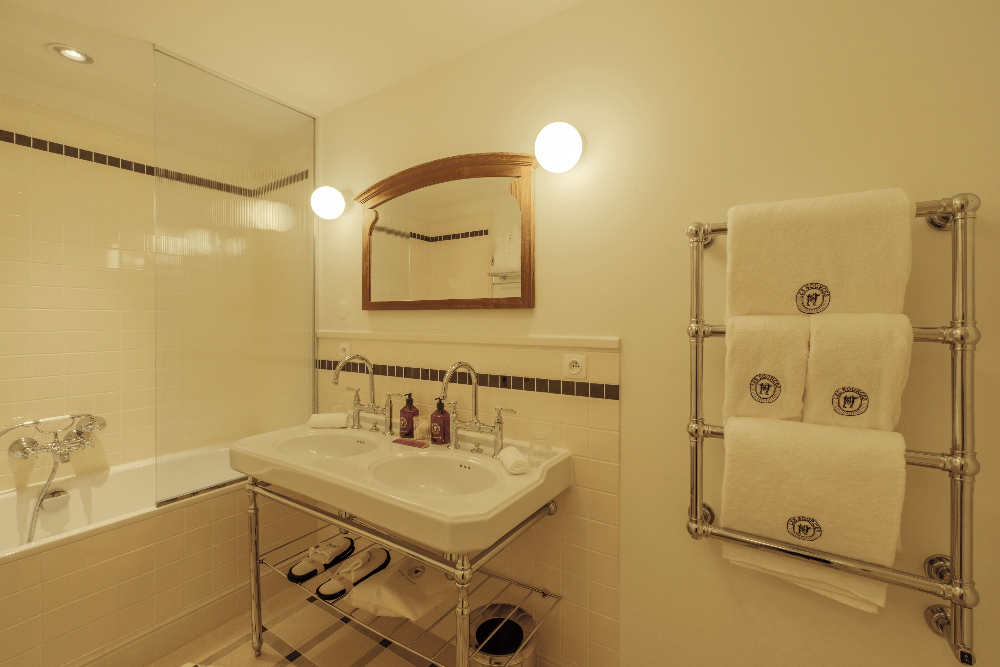 Un baño con bañera, dos lavamanos, un espejo y un perchero para toallas.
