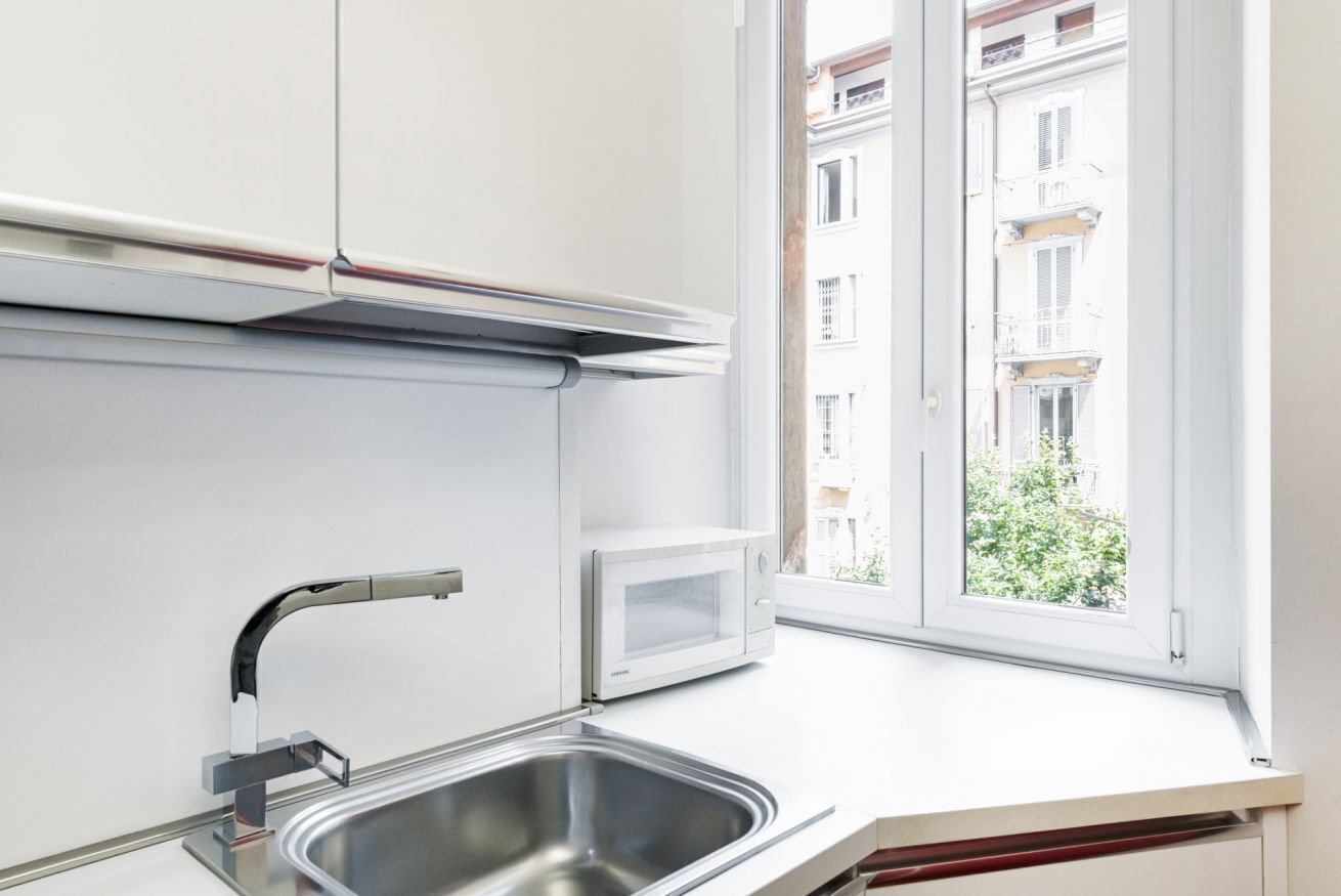 A modern kitchen with a stainless steel sink, a microwave, and a window overlooking a residential area.