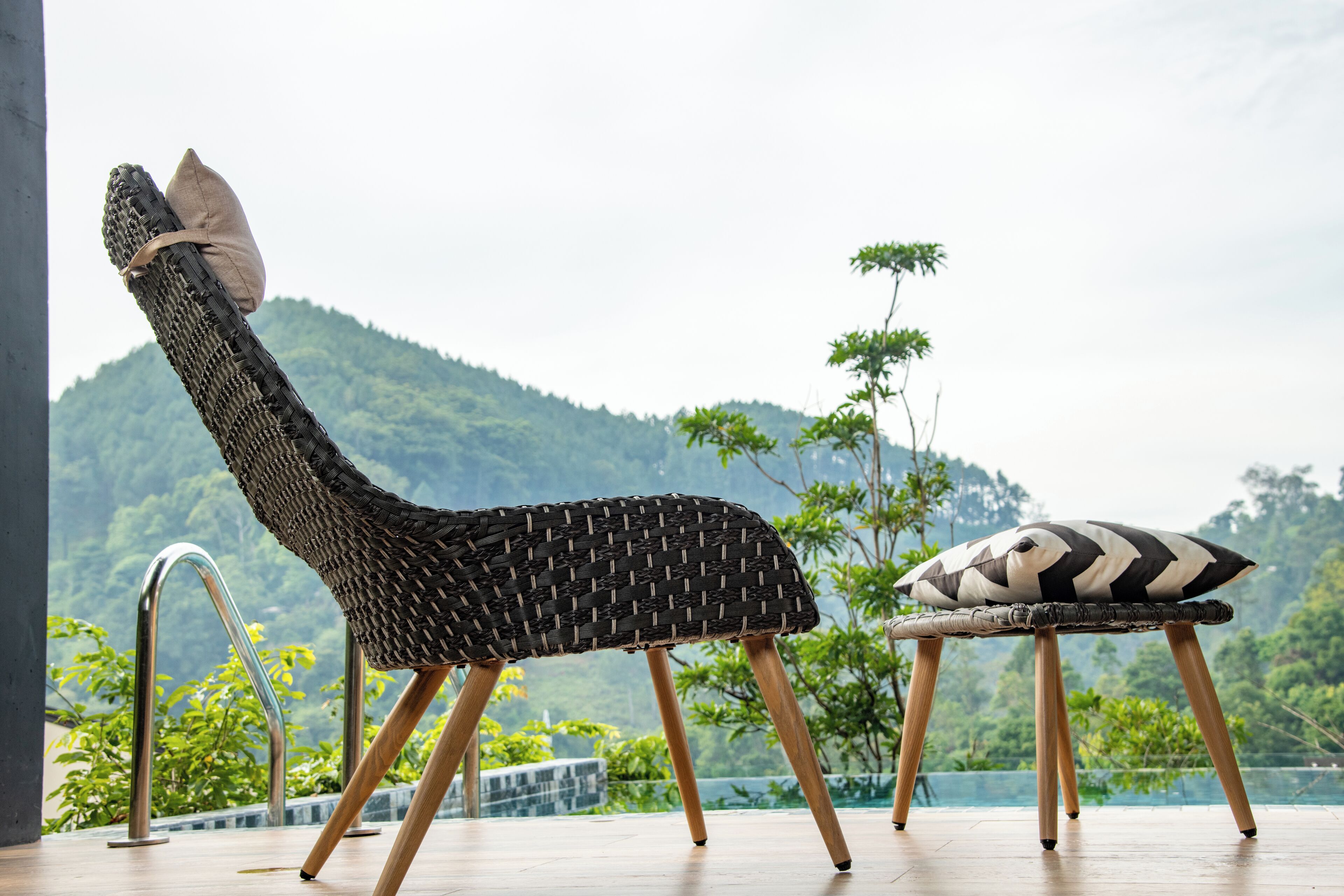Ein Korbsessel mit Kissen, platziert auf einer Holzterrasse mit Blick auf eine Berglandschaft.