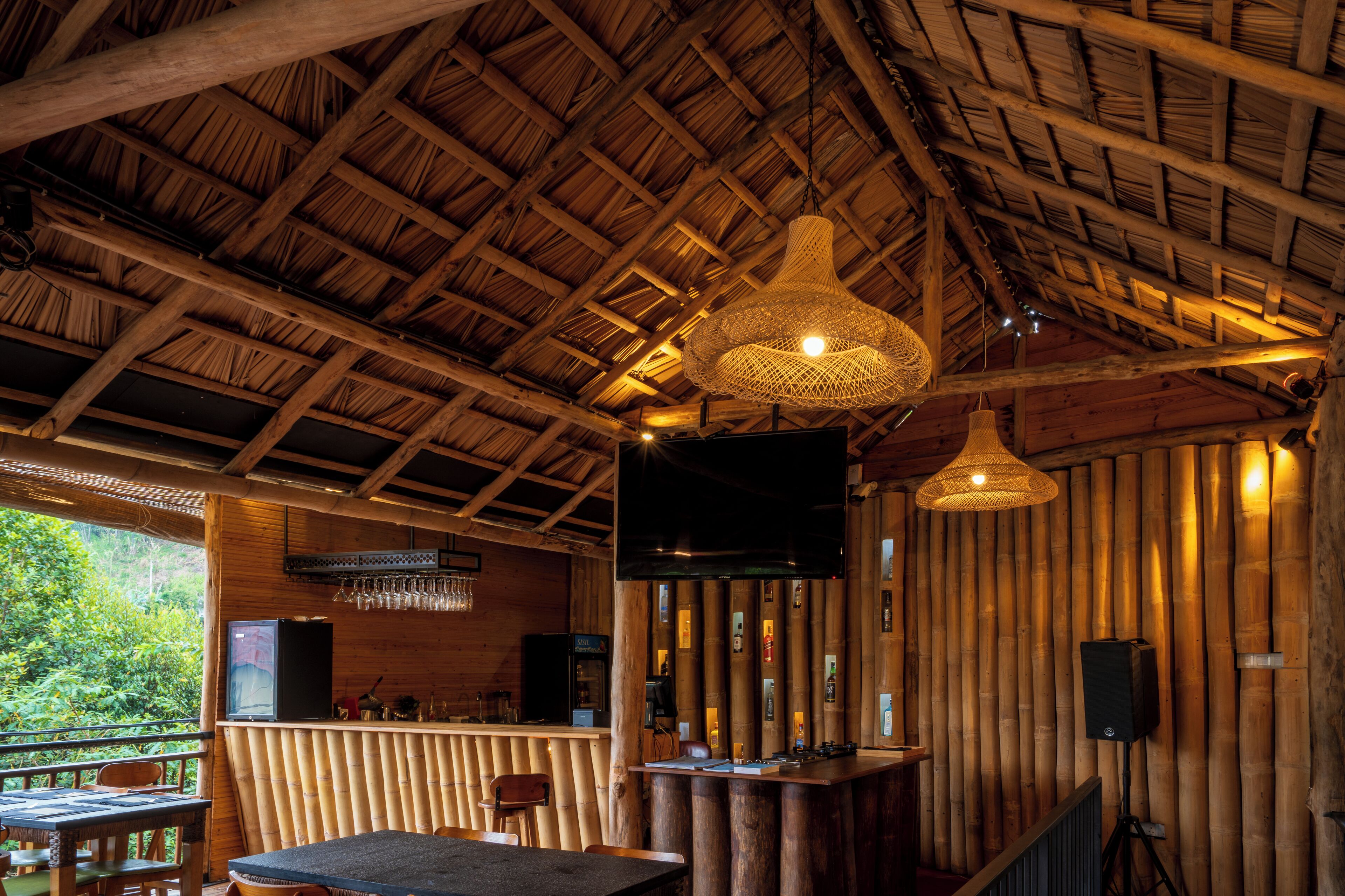 A rustic wooden interior with a thatched roof, a bar area, and a large woven light fixture.