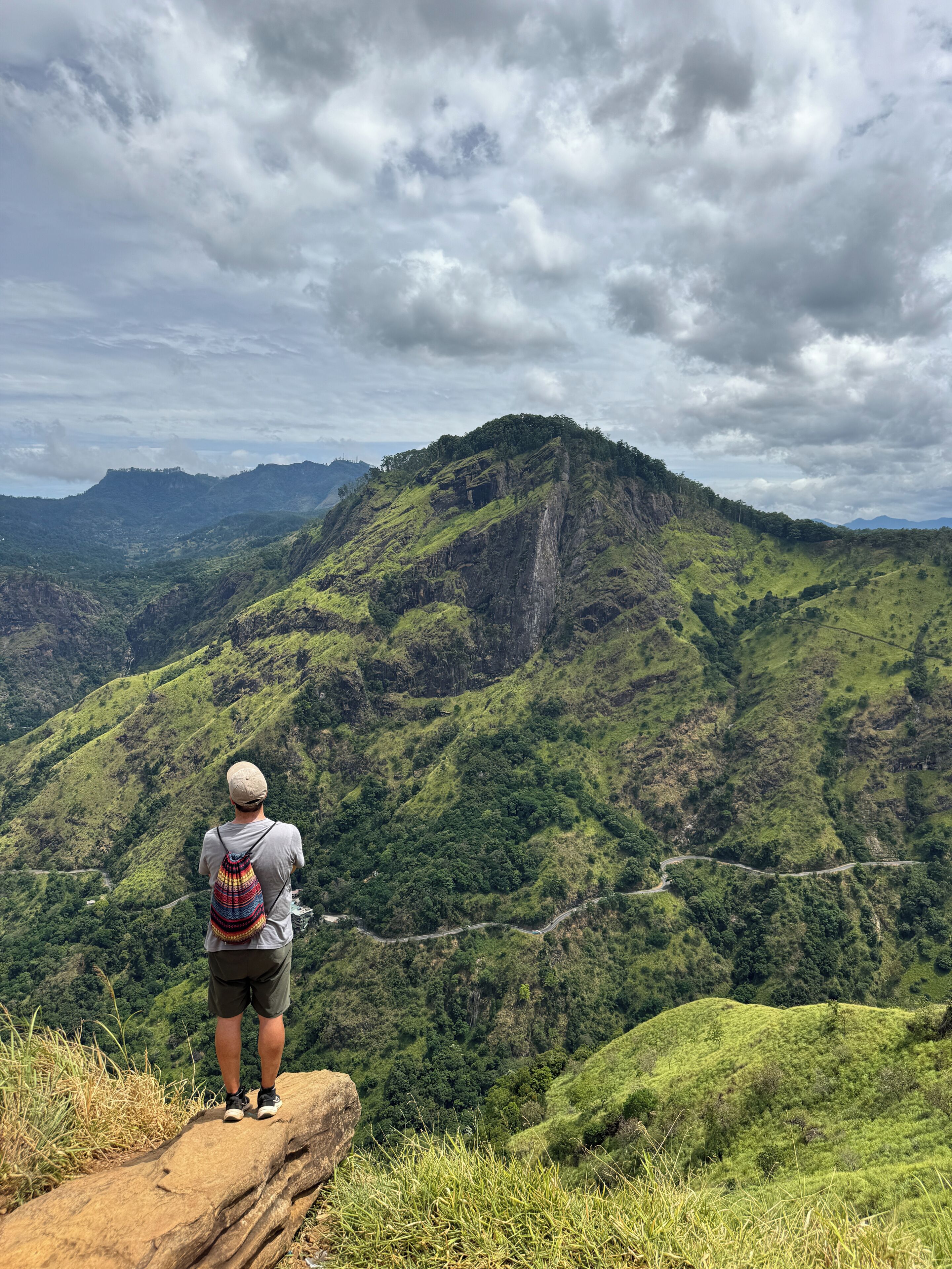 Una persona parada sobre un afloramiento rocoso, con vistas a un paisaje montañoso y un camino sinuoso.