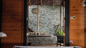 A wooden room with a bed, a stone wall, and a small table with a chair. - O2 Villas Ella (Ella)