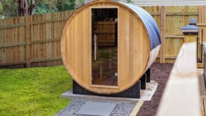 A wooden barrel-shaped structure with a door, situated on a gravel path with a wooden fence in the background.