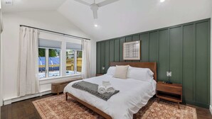 A bedroom with a large bed, a wooden nightstand, a ceiling fan, and a window with curtains.