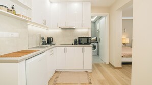 A compact kitchen with white cabinets, a microwave, a coffee maker, and a washing machine in the background. - Plantaea Studio - Athens Escape  (Athens)