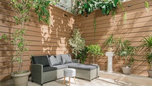 A sunlit patio with a wicker sofa, a small ottoman, and various potted plants. - Plantaea Studio - Athens Escape  (Athens)