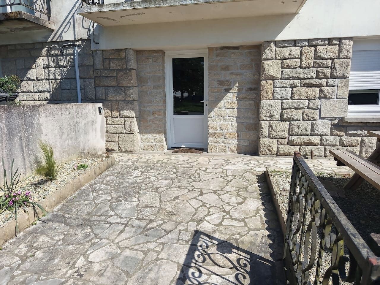 A stone-paved entrance to a building with a metal gate, a door, and a small outdoor seating area.