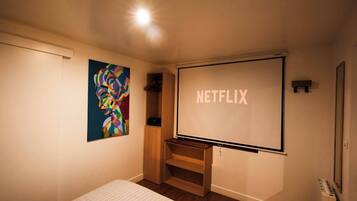 Ein Zimmer mit einem großen Bildschirm, auf dem "NETFLIX" angezeigt wird, einem farbenfrohen abstrakten Gemälde an der Wand und einer Holzschrank.